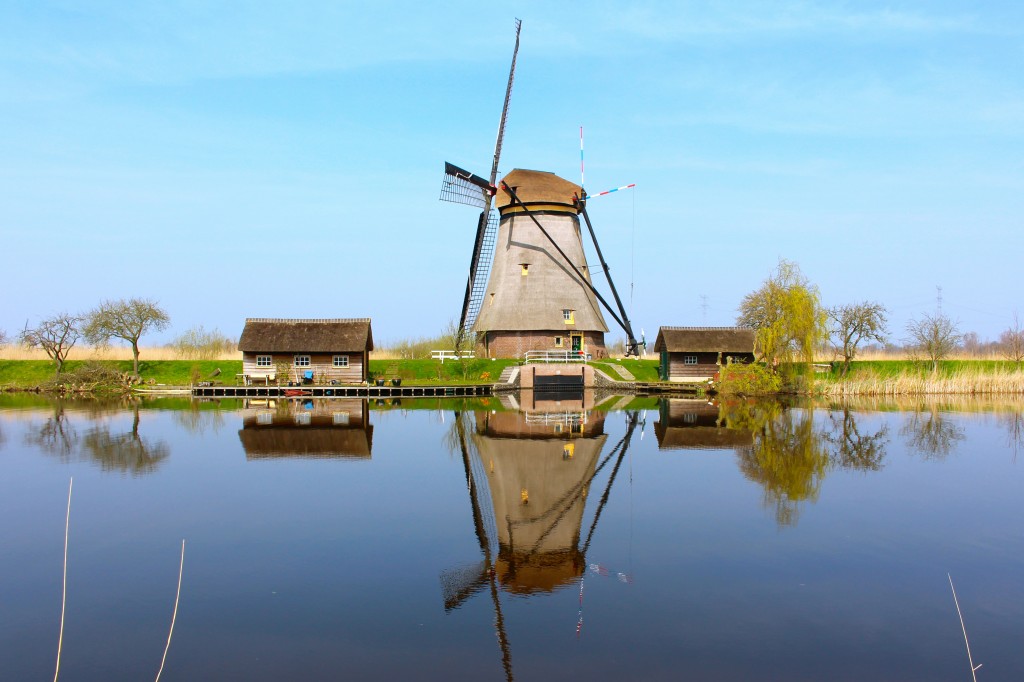 A freestanding windmill on the water with two smaller houses around it in Kinderdijk Holland