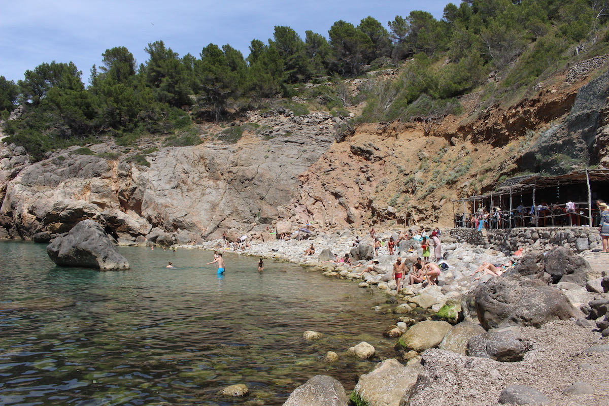 Locals and tourists perch on the rocks at the pebbled beach of Cala Deia, Mallorca