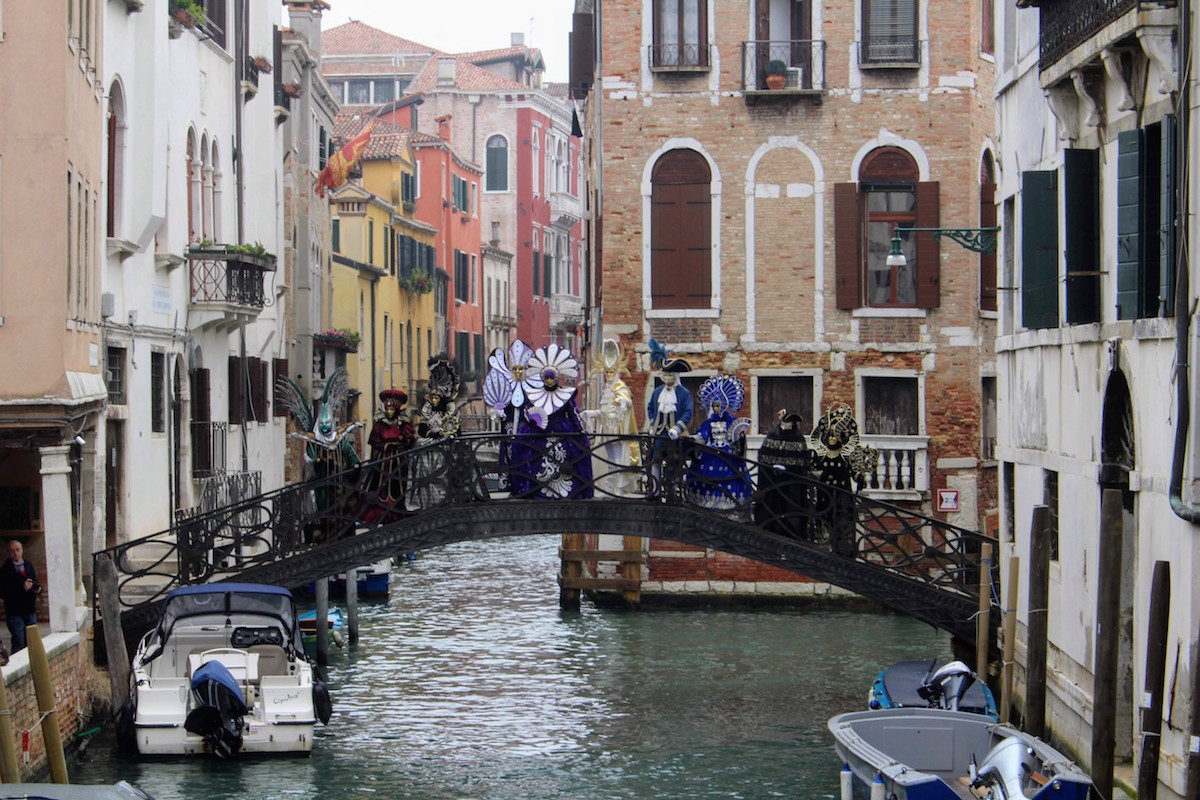A row of people dressed in traditional Carnival costumes in Venice pose on a bridge