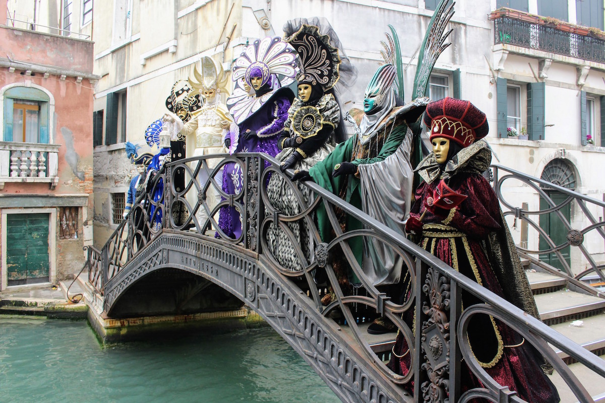 A row of people dressed in traditional Carnival costumes in Venice pose on a bridge