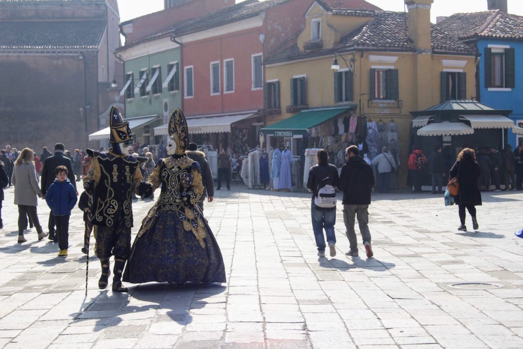 A couple dressed in traditional Venetian costumes and masks strolling the streets of Burano