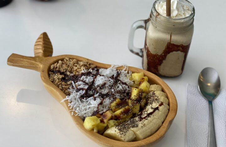 A smoothie bowl in a wooden pear shaped bowl with a frappuccino