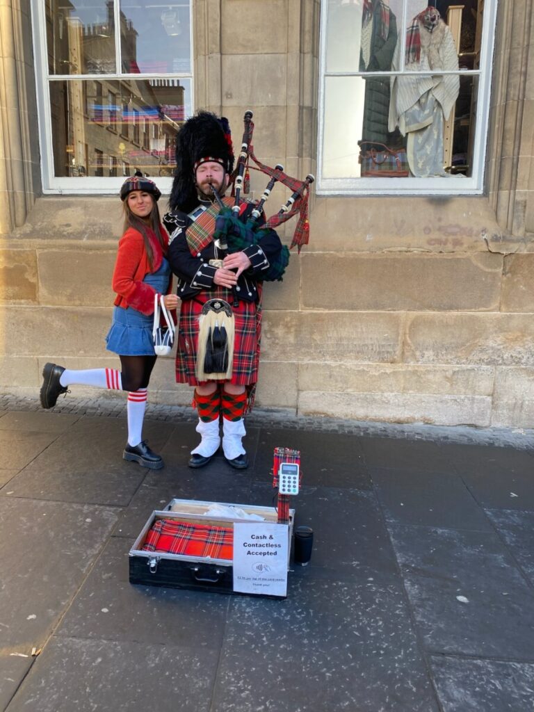 Alisa posing with a Scottish man in traditional dress with bagpipes