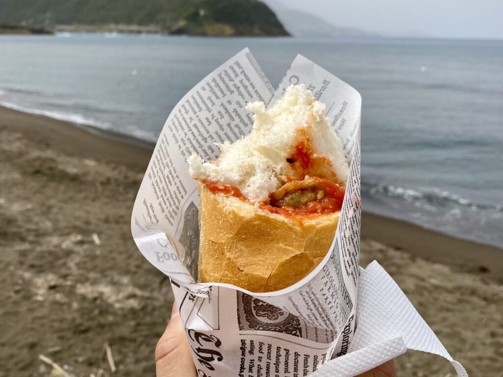 A meatball and eggplant parmigiana sandwich at the beach in Spiaggia della Chiaiolella, Procida, Italy